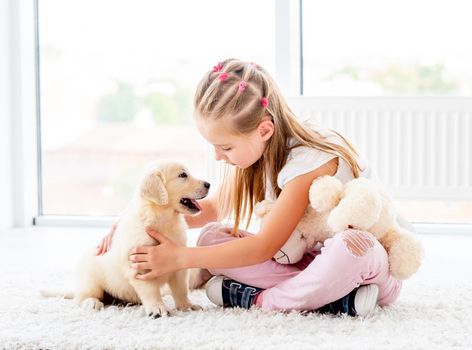 Lovely little girl petting retriever puppy in house