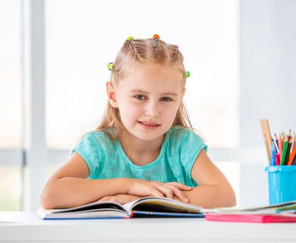 Beatiful little schoolgirl is sitting calmly in classroom, with book open