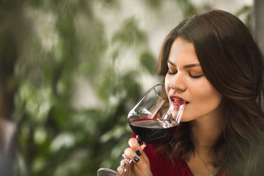 A beautiful girl presents a glass of red wine to her lips