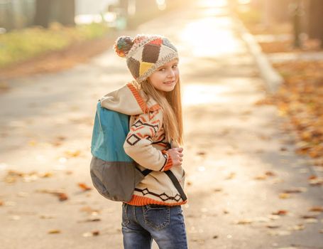 Nice little girl going to school through autumn park