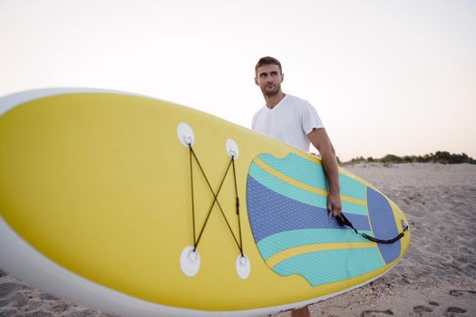 Young man carrying sup board after water surf session, close up