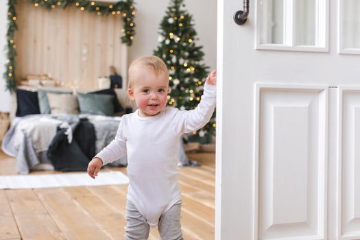 Adorable little child standing at bedroom with Christmas tree.