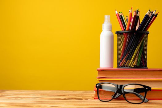Back to school concept with stationery in cup and hand antiseptic spray against yellow background