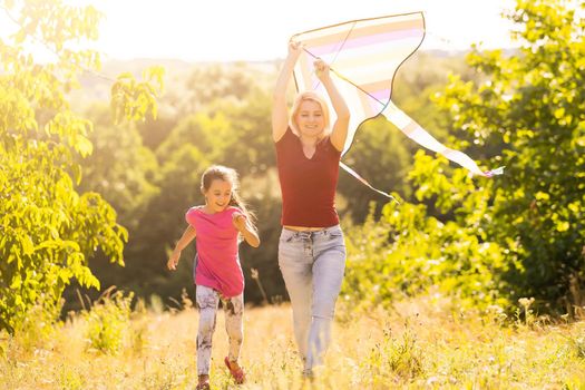 happy family mother and child run on meadow with a kite in the summer on the nature