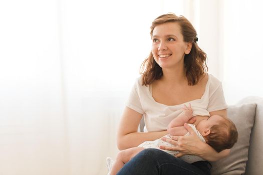 Cheerful young woman breastfeeding infant child at home.