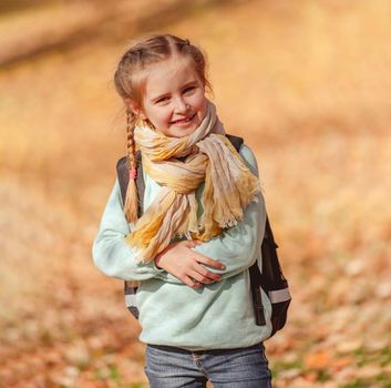 Smiling little girl with backpack on yellow leaves background