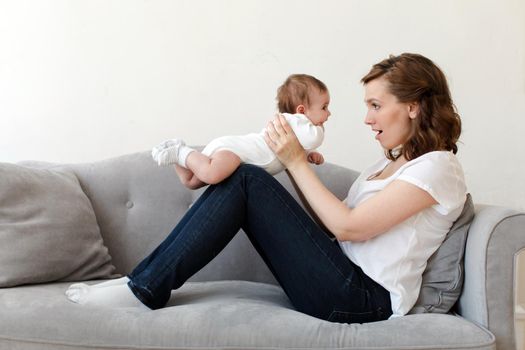 Side view of woman sitting on couch at home with newborn baby on hands
