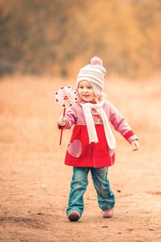 little smiling girl on autumn landscape with pinwheel toy