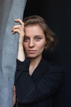 portrait of young caucasian woman with short hair posing in black suit jacket, holding curtain. closeup shot of pretty girl. short-haired attractive female poses in studio