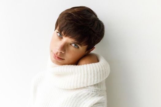 Portrait of young charming woman with short haircut posing in white sweater looking at camera.