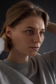 portrait of caucasian woman with short hair posing in gray sweatshirt on black studio background. close up shot of pretty girl. attractive pensive young female poses in studio