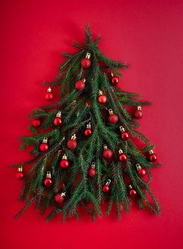 Christmas tree made of green coniferous branches on a red background. Christmas background with place for text. Christmas holiday concept. Ball toys.