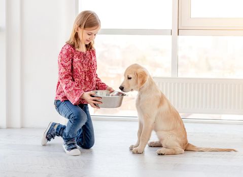 Lovely little girl giving food to her beautiful dog indoors