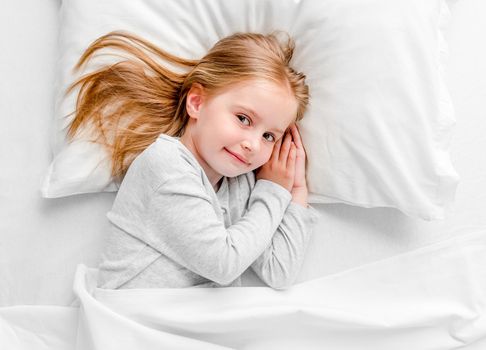 cute smiling little girl woke up in white bed