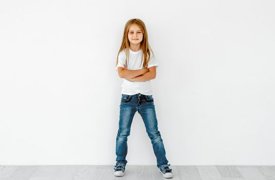 Young happy girl with crossed hands and serious face in white t-shirt and jeans isolated on white background with copy space