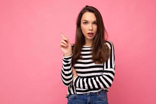 Shot of young positive self-confident happy attractive brunette woman with sincere emotions wearing casual striped longsleeve isolated on pink background with empty space and thinking.