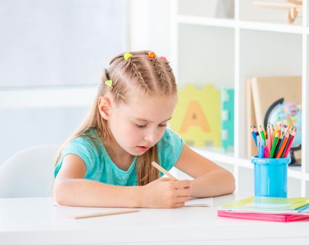 School aged girl writing with pencil in classroom