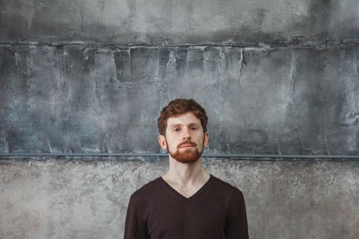 Portrait of young bearded man looking at camera while standing at concrete wall.