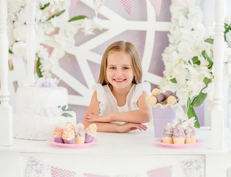 Little cute blond girl holding a sweet cake on the background of pretty decorated candy bar