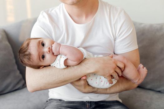 Anonymous man holding and embracing adorable baby while sitting on comfortable couch in living room