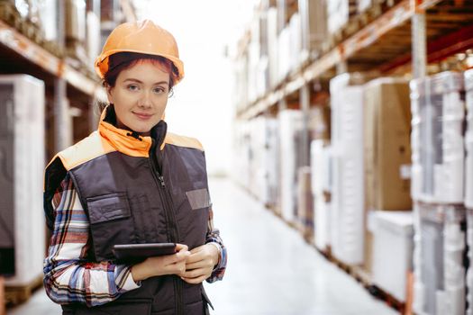 Woman with a clipboard in her hands is checking inventory levels in a warehouse. Smiling girl scrolling on digital tablet in a large warehouse time delivery concept photo.