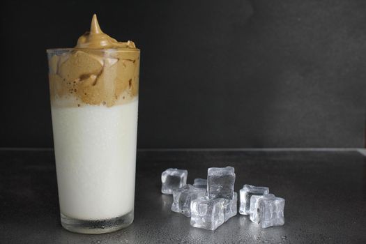 Dalgon coffee milk with coffee coffee foam and ice in a glass on a black dark background with a place to text a trendy drink.