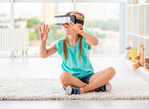 Little girl wearing virtual reality glasses in playing room