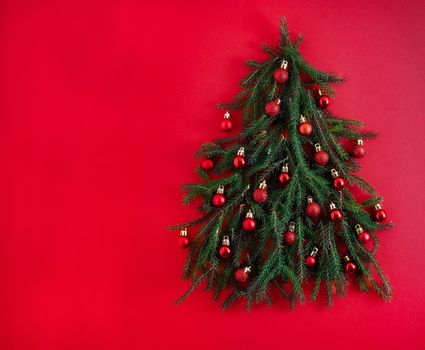 Christmas tree made of green coniferous branches on a red background. Christmas background with place for text. Christmas holiday concept. Ball toys. Copy space.