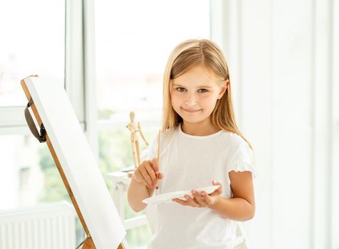 Cute little girl paints on canvas in a spacious white room