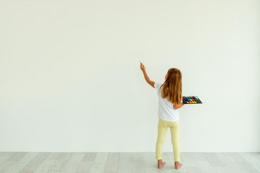 Little girl painting on white wall indoors. view from the back