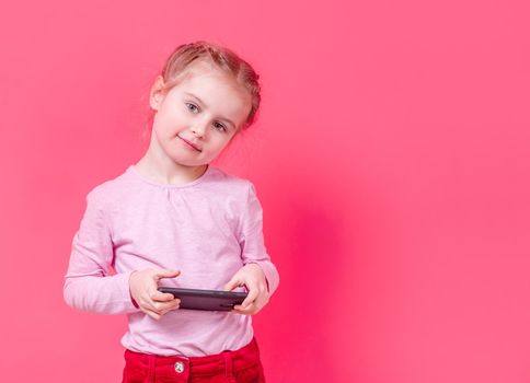 Adorable stylish small girl using smartphone over pink background