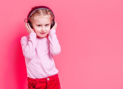 Modern little girl posing in headphones over rose background