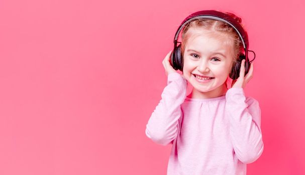 Modern little girl posing in headphones over rose background