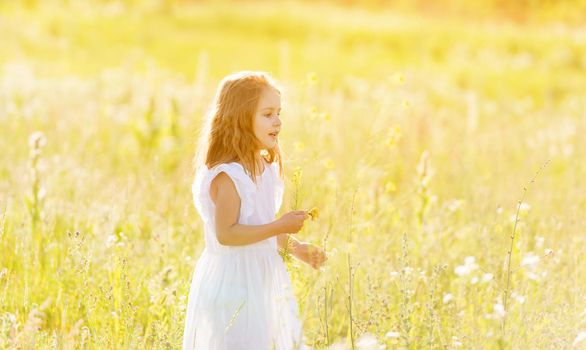 Adorable little girl posing in white dress in garden looking to the side with curiosity