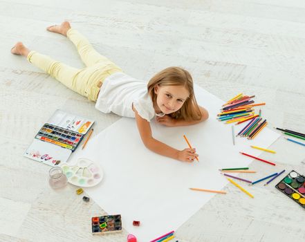 little cheerful girl draws lying on the floor