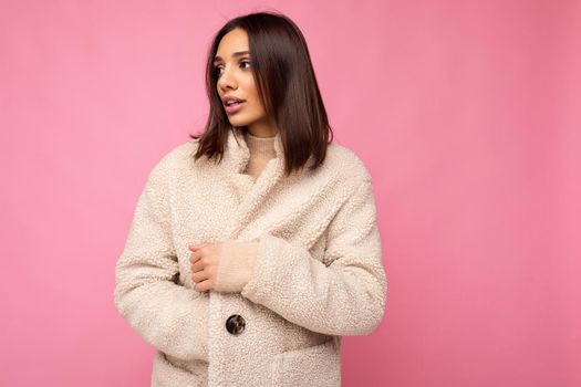Portrait of attractive self-confident positive good-looking stylish young brunette woman wearing winter beaige warm coat isolated on pink background with free space. Fashion concept.