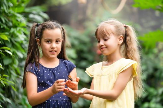 Two little sisters holding a butterfly in their hands. Children exploring nature. Family leisure with kids at summer.