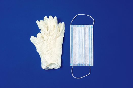 Medical gloves and surgical protective face mask on dark blue background. Coronavirus concept