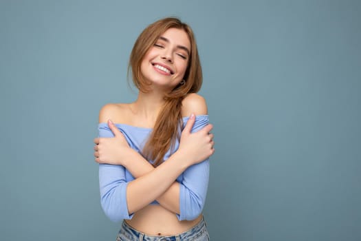 Smiling young positive beautiful dark blonde woman with sincere emotions isolated on background wall with copy space wearing casual blue crop top. Happy concept.
