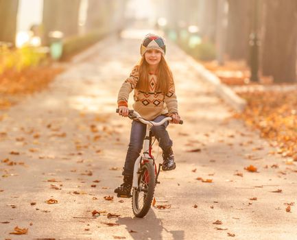 Happy school girl riding bike in autumn park