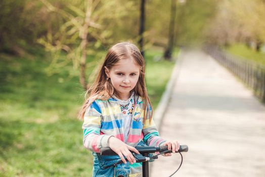 Small happy toddler girl with cool modern scooter on blurry background