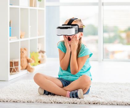 Amazed schoolgirl watching cool movie in headset of virtual reality