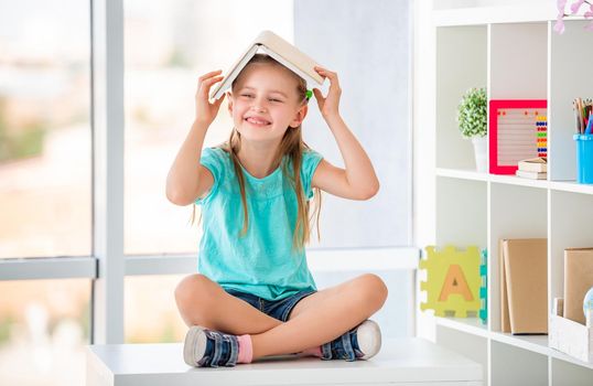 Girl playing with textbook sitting on desk in school