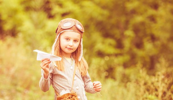 cute little girl in helmet pilot with paper airplane outdoors