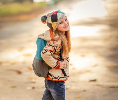 Nice little girl going to school through autumn park