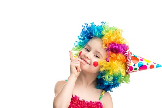 Funny little girl in multicolored clown wig pointing up on blank space, isolated on a white background, space for text
