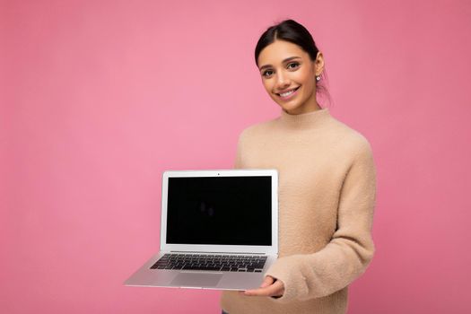 Photo of beautiful young woman holding computer laptop looking at camera isolated over colourful background.