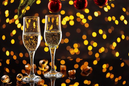 Two glasses of champagne and Christmas baubles on shiny bokeh lights background