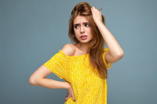 Young sad upset beautiful dark blonde woman with sincere emotions isolated on background wall with copy space wearing stylish summer yellow dress. Sorrowful concept.