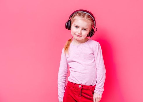 Modern little girl posing in headphones over rose background